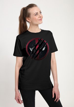 Kvinde iført sort t-shirt med slidt rød og sort cirkulært grafik og kløemærker, der kigger let opad mod højre.