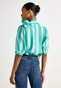 Grön och ljusblå randig blus med puffärmar, knappdetaljer och en rosett vid kragen, som kombineras med högmidjade jeans.