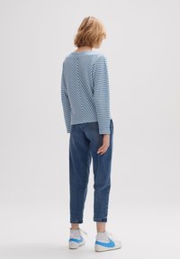 Paskowany sweter dziany w kolorze niebieskim i białym z wzorem w kształcie litery V, zestawiony z ciemnoniebieskimi dżinsami i białymi trampkami z niebieskimi akcentami.