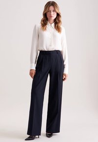 Hvid skjorte med lange ærmer og knapper, kombineret med højtaljede, marineblå bukser med vide ben. Glat stof med en skræddersyet pasform og et elegant snit.