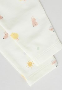 Leggings doux de couleur crème avec un motif ludique d'animaux et d'illustrations de soleil dans des teintes pastel, offrant une texture de tissu lisse.