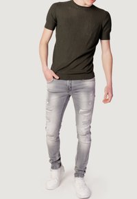 T-shirt a maniche corte a righe verde oliva scuro con taschino sul petto, abbinato a jeans skinny grigio chiaro strappati e sneakers bianche.
