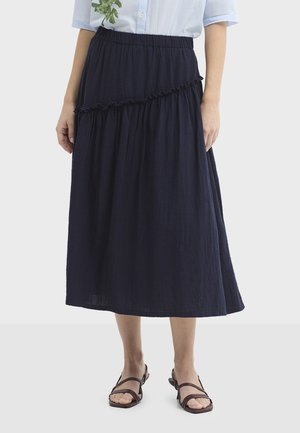 Niebieska, warstwowa spódnica midi wykonana z teksturowanej tkaniny, z elastycznym paskiem i falbaną przy szwie. Noszona z brązowymi sandałami.