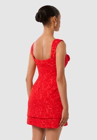 Robe rouge en tissu texturé, à la coupe ajustée, avec un décolleté carré et des manches courtes, dotée d'un ourlet superposé.