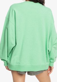 Sudadera verde de gran tamaño hecha de material suave, con hombros caídos y puños acanalados; detalles mínimos, corte casual y estilo relajado.