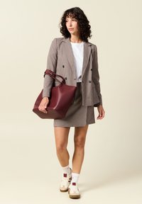 Tarkistettu bleiseri ja hameyhdistelmä ruskeassa ja valkoisessa, punamarjainen laukku; malli pukeutuu valkoiseen paitaan ja vaaleisiin lenkkarit, joissa on vaaleanpunaisia yksityiskohtia.