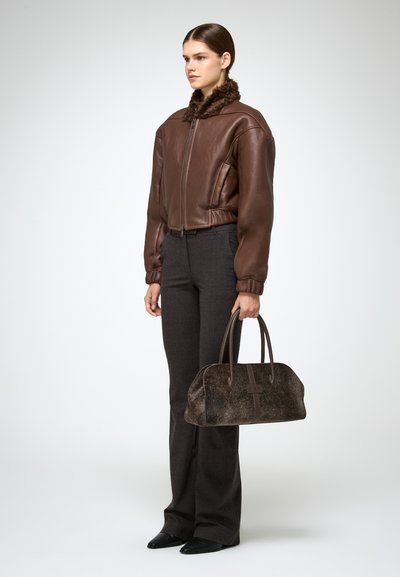 Bruine leren bomberjack met een bontkraag, gecombineerd met donkere flare-broek en een gestructureerde donkerbruine handtas. Gestructureerde stofaccenten.