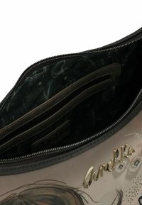 Borsa con scomparto non chiuso, che mostra la fodera in tessuto stampato scuro, tasca interna con zip e logo in metallo dorato "Anekke" sulla superficie beige.
