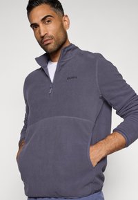 Φλις πούλεν σε σκούρο γκρί με μισό φερμουάρ, πλαϊνές τσέπες και κεντημένο λογότυπο "BORG" στο στήθος. Μαλακή υφή, χαλαρή εφαρμογή.