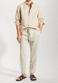 Camisa de lino en color beige claro con mangas arremangadas, combinada con pantalones ajustados a juego y sandalias marrones con un diseño de tiras.