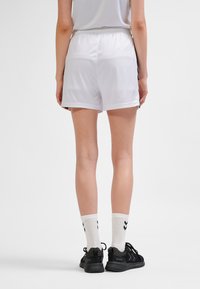 Weiße Sportshorts mit elastischem Bund, glatter Textur und kurzem Schnitt. Kombiniert mit schwarzen Sneakers und weißen Socken mit schwarzen Streifen.