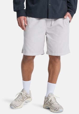 Pantaloncini in velluto a coste grigio chiaro con una vestibilità comoda, tasche laterali e lunghezza a metà coscia, abbinati a scarpe da ginnastica beige e calzini bianchi.