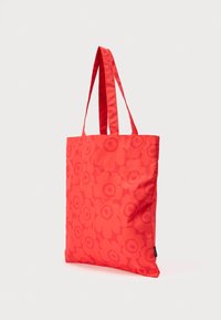 Κόκκινη τσάντα ώμου με μακριά χερούλια που διαθέτει έντονο λουλουδάτο σχέδιο με μεγάλα λουλούδια με κυκλικούς πυρήνες σε απλό φόντο.