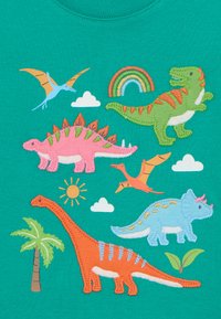 Teal skjorte med fargerike dinosaur-applikasjoner: rosa stegosaurus, grønn T-rex, blå triceratops, med detaljer av skyer, sol og palmetre.
