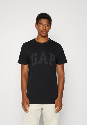 T-shirt en coton noir avec un grand logo "GAP" gris foncé sur la poitrine. Des manches courtes et un col rond complètent le design.
