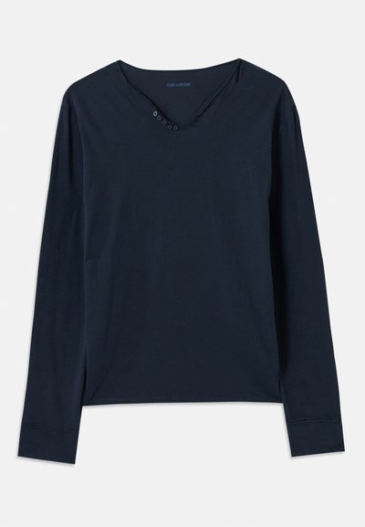 Ilgām piedurknēm, tumši zila T-kreklu no mīkstas kokvilnas. Iespējo V veida kakla izgriezumu ar piecām pogām un diskretām sānu šķirbēm apakšmalā.