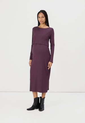 Ribbed, long-sleeve, purple maternity dress with a fitted silhouette, featuring a cropped top section and floor-length skirt. Worn with black boots.