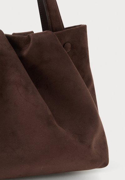 Borsa tote in suede marrone con texture morbida, design pieghevole e dettaglio a pulsante circolare, dotata di spallacci robusti.