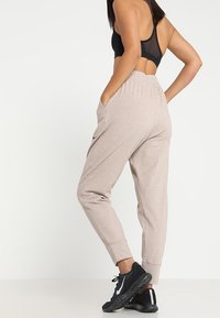 Pantalones jogger beige hechos de material suave, con cintura elástica, bolsillos laterales y tobillos ajustados, combinados con zapatillas deportivas negras.