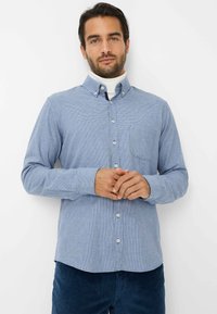 Camicia a scacchi blu con bottoni, tasca, maniche lunghe e orlo arrotondato. Tessuto leggero con una sottile texture.