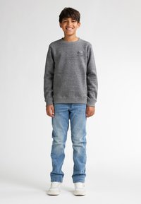 Grauer Sweatshirt mit Rundhalsausschnitt, gerippten Bündchen und hellblauen Jeans. Weiße Sneakers vervollständigen das Outfit. Schlichtes Design ohne sichtbare Muster.