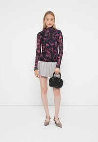 Top de manga longa em roxo escuro com padrão abstrato em rosa, combinado com uma saia plissada cinza e uma pequena bolsa preta texturizada.