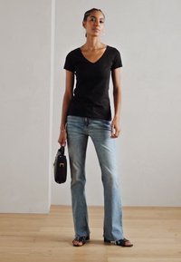 Black V-neck t-shirt, paired with light blue flared jeans. Additional accessories include a small black handbag and black sandals.