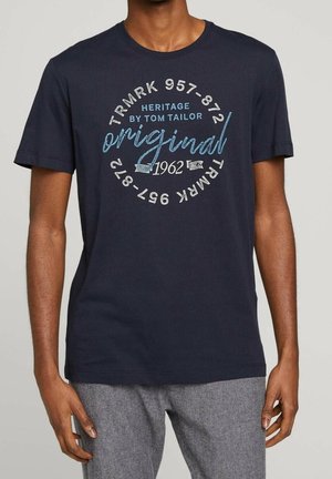 Marineblå bomulds T-shirt med cirkulært grafisk tryk. Teksten inkluderer "Heritage by Tom Tailor," "original," og året "1962" i forskellige farver.