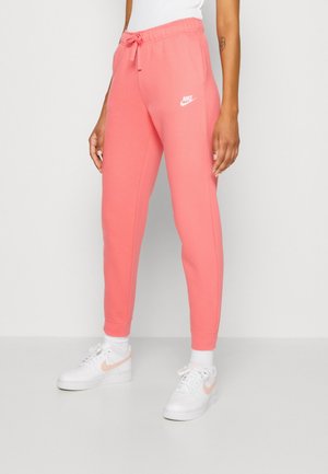 Roze Nike-sweatpants met elastische tailleband en trekkoord, tapered pijpen en logo-detail. Gecombineerd met witte sneakers en sokken.