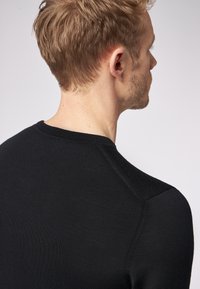 Maglione nero lavorato a maglia con collo rotondo, texture liscia e maniche raglan, incentrato sul profilo posteriore di chi lo indossa.