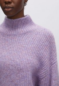 Lila gestrickter Pullover mit Rollkragen, gerippter Struktur und leicht lockerer Passform. Weiches Material mit subtilen Farbvariationen.