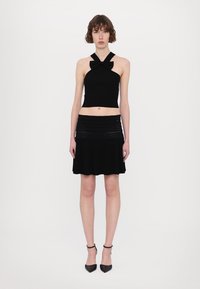 Melna halter stila crop top ar bantītes detaļu, apvienota ar plisētu melnu svārku. Materiāli izskatās pieguloši ar mīkstu tekstūru. Melni papēži noslēdz izskatu.