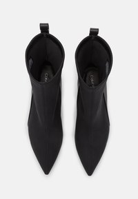 Par av svarta spetthåriga ankelboots med dragremmar bak, sedd uppifrån på en vit bakgrund.