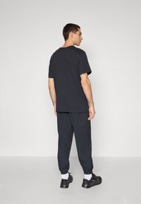 Camiseta de algodón negra con mangas cortas, combinada con pantalones jogger oscuros, que presentan puños elásticos y zapatillas negras con detalles amarillos.