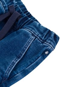 Pantaloni in denim di colore blu profondo, con cintura elastica e cordoncino. Presentano un piccolo tag con logo e tasche strutturate.