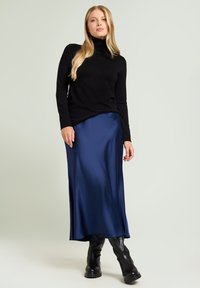 Czarny sweter w golfie zestawiony z elegancką, granatową satynową maxi spódnicą. Modelka nosi czarne, wysokie na kolana botki, co podkreśla warstwowy wygląd.