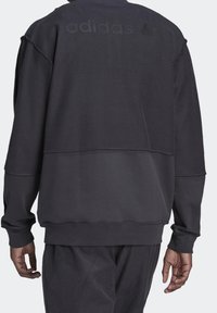 Svart sweatshirt med långa ärmar, med en texturerad övre sektion, ribbade manschetter och en horisontellt indelad design. Diskret branding på baksidan.