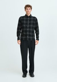 Black and grey plaid flannel shirt with buttons, long sleeves, and a curved hem, paired with black pleated trousers and black shoes.