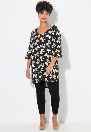 Sort tunika med creme- og tan-blomster mønster, V-hals med perledetaljer, oversized pasform, klokkeslæt, parret med sorte leggings og nude hæle.