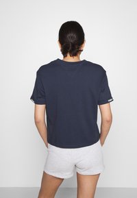 Marineblå kortärmad t-shirt i bomullstyg med rund halsringning. Har en logotypdetalj på ärmen. Sammanställd med gråa shorts.