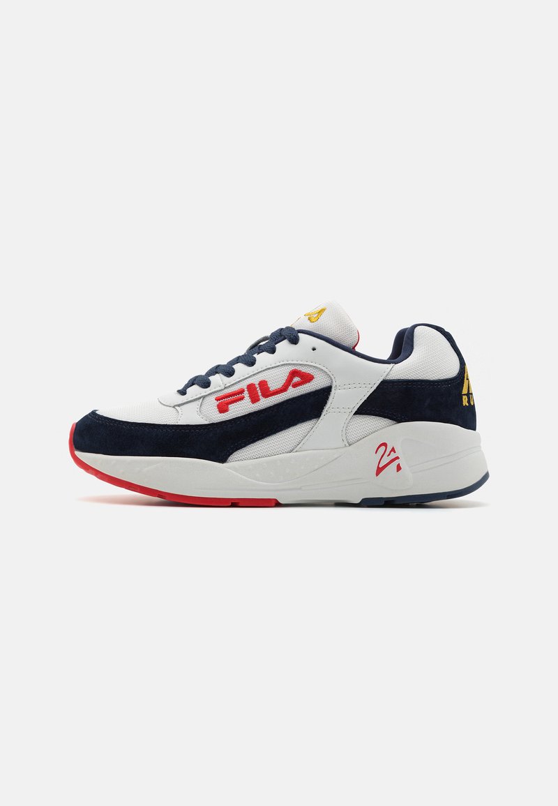 Hvit sneaker med marineblå semsket skinndetaljer, rød såle og med en dristig rød FILA-logo. Har blå snørebånd og strukturert stoff på overdelen.