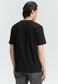 Schwarzes kurzärmeliges T-Shirt aus Baumwolle mit Rundhalsausschnitt und glatter Textur, aus einem hinteren Blickwinkel präsentiert und mit einem schlichten Design.