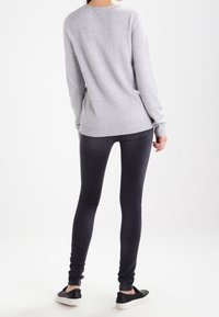 Jasnoszary sweter z długimi rękawami, ribbowym wykończeniem i luźnym krojem, w połączeniu z ciemnymi skinny jeansami i czarnymi butami na slip-on.