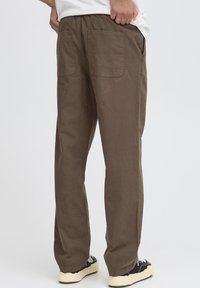 Pantaloni di cotone marroni con vestibilità rilassata, caratterizzati da una vita con coulisse, due tasche posteriori e una texture liscia, mostrati di schiena.