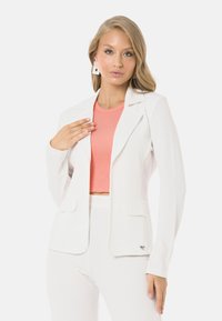 Weißer gerippter Blazer mit Reverskragen und zwei Vorderentaschen, über einem rosa gerippten Crop-Top getragen. Das Model zeigt eine schlanke, figurbetonte Silhouette.