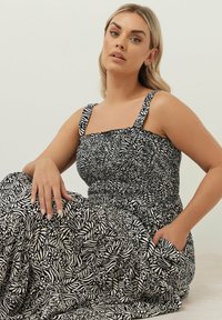 Svart- och vitt mönstrad klänning med smockad byst och breda band, med en flödande kjol och sidofickor.