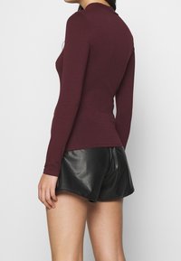 Viininpunainen pitkähihainen paita korkealla kaula-aukolla, yhdistetty mustiin nahkashortseihin, joissa on istuva malli ja sileä pinta.