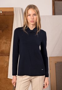 Marinblå långärmad topp med polokrage och figurnära passform, gjord av ett mjukt tyg. Har en diskret logotypdetalj vid fållen.