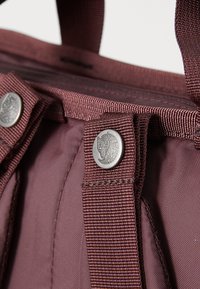Bolso tote color burdeos con tela texturizada, que presenta herrajes plateados y un emblema de caballo, exhibiendo costuras reforzadas en las correas para el hombro.