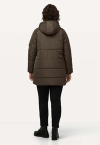 Chaqueta acolchada marrón con capucha, con detalles de acolchado y mangas largas. Combinada con jeans negros y botines negros.